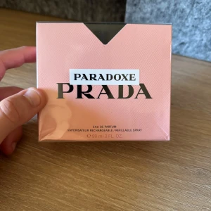 Prada Paradoxe EDP 90ml - Säljer en elegant Paradoxe Eau de Parfum från Prada. Förpackningen är i en mjuk rosa färg med stilren design och tydlig logotyp. Flaskan är påfyllningsbar vilket gör den både lyxig och praktisk. Perfekt för den som älskar exklusiva dofter.