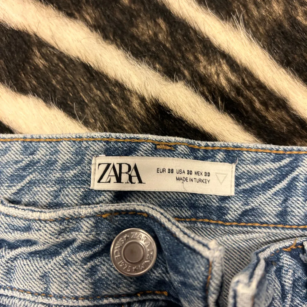 Säljer ett par snygga blå jeans från Zara i storlek 30. De har en cool slitning på framsidan som ger dem en trendig look. Jeansen har en knappgylf och är i en klassisk straight fit. Perfekta för både vardag och fest!. Jeans & Byxor.