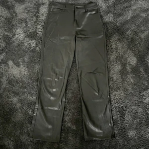 Svarta skinnbyxor från BikBok - Säljer ett par snygga svarta skinnbyxor från BikBok i storlek 42. Byxorna har en straight passform och är högmidjade, vilket ger en stilren look. Perfekta för både fest och vardag! De har knappar och dragkedja framtill för enkel på- och avtagning.