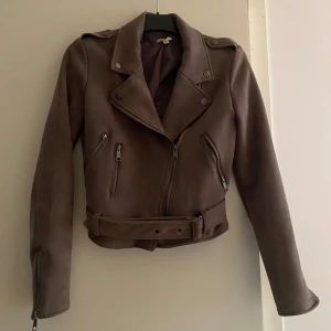 Jacka i mockaimitation  - Jacka i mockaimitation från Nelly.  Mörk beige/ brun. Använd fåtal gånger, mycket fint skick.  Strl 34.