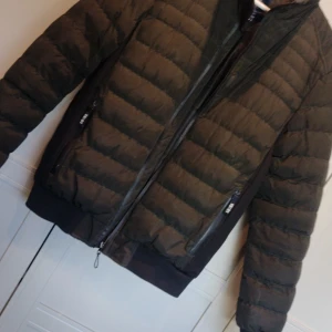 Svart pufferjacka från Michael Richman - Säljer en snygg och varm Kaki pufferjacka från Mell Richman. Jackan har en dragkedja framtill och är perfekt för kyliga dagar. Den är i storlek S och passar bra för både höst och vinter. Perfekt för dig som vill hålla stilen när det är kallt ute!