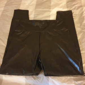Svarta leggings - Säljer ett par svarta leggings i läderimitation i storlek L. De är gjorda av 90% polyester och 10% elastan, vilket gör dem stretchiga och bekväma. Perfekta för en cool och stilren look! Helt nya! 