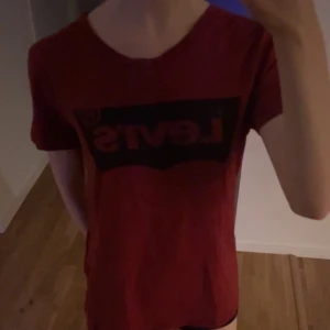 Röd t-shirt från Levi's - Säljer en röd t-shirt från Levi's med det klassiska logotyptrycket i svart på bröstet. Som man kan se på sista bilden har tröjan ett litet hål längst ner på tröjan som knappt syns. 