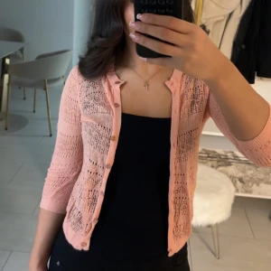 korall kofta - Säljer en söt rosa kofta från MNG Basics. Koftan har ett öppet stickat mönster och trekvartsärmar. Perfekt för att lägga till en färgklick till din outfit. Den har knappar framtill och är tillverkad i ett lätt material. 