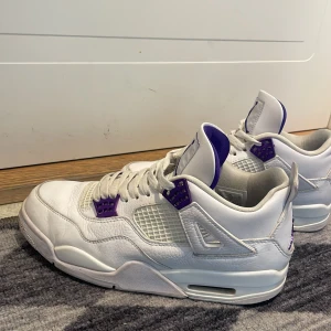Vita och lila Nike Air Jordans - Säljer ett par vita Nike Air Jordans med lila detaljer. Skorna har en klassisk design med snörning och den ikoniska Jumpman-loggan. Perfekta för dig som vill ha en stilren och sportig look.