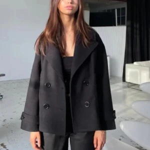 Svart kappa med knappar - Snygg svart kappa med dubbelknäppning och bred krage. Jackan har långa ärmar och en stilren design som passar perfekt för kyligare dagar. Perfekt för dig som vill ha en klassisk look.