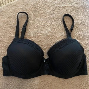 Svart bh - Säljer en elegant svart bh från Trofé med spetsdetaljer och en liten pärla framtill. Bh:n har justerbara axelband och en hakknäppning bak. Materialet är en blandning av polyamid och polyester för en bekväm passform.😻Så snygg💋
