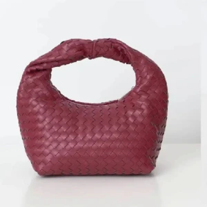 Vinröd flätad handväska - Snygg vinröd handväska med flätat mönster och dragkedja. Perfekt för att ge en touch av stil till din outfit. Den har en unik form och är lätt att bära med sig.
