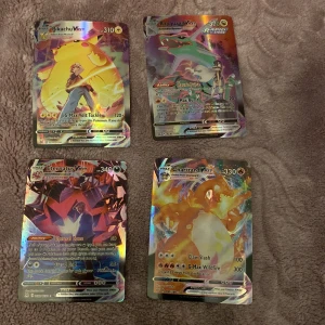 Pokémon VMAX-kort - Säljer fyra Pokémon VMAX-kort med färgglada och detaljerade illustrationer. Kortens framsidor visar olika Pokémon i dynamiska poser, medan baksidorna har den klassiska blå designen med en Pokéball i mitten. Perfekt för samlare eller spelentusiaster!