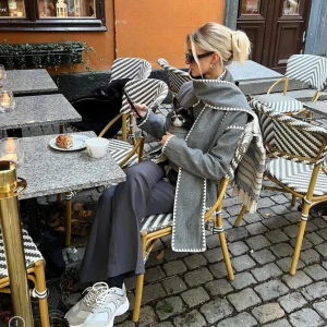 Grå kappa med vit kant - Snygg grå kappa med vit kantdetalj. Den har en unik design med en stor krage och långa ärmar. Perfekt för att hålla sig varm och stilren under kyliga dagar.