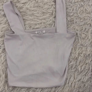 Vit ribbad linnetopp från Amisu - Säljer en stilren vit ribbad linnetopp från Amisu. Toppen har breda axelband och en enkel design som passar perfekt till sommaren. Perfekt för en avslappnad och trendig look.