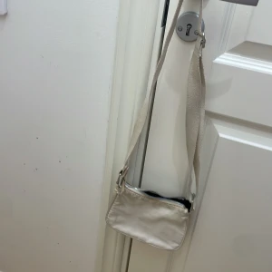 Beige axelväska med dragkedja - Snygg beige axelväska med justerbar axelrem och dragkedja upptill. Perfekt för att bära dina nödvändigheter med stil. Enkel och stilren design som passar till många olika outfits.