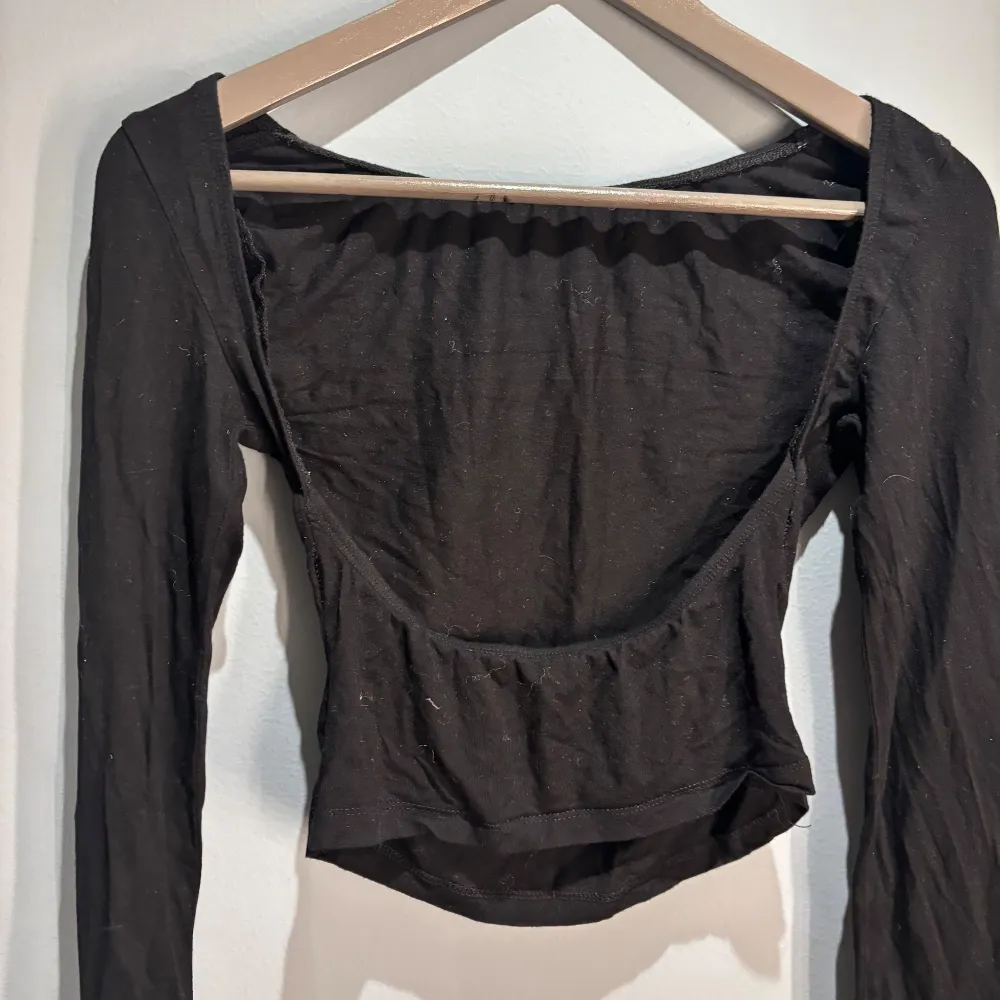 Snygg svart långärmad topp med öppen rygg. Perfekt för en stilren look. Toppen är i ett mjukt och stretchigt material som ger en bekväm passform.. Yläosat.