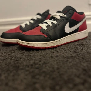 Nike Air Jordans i svart, röd och vit - Snygga Nike Air Jordans i en klassisk färgkombination av svart, röd och vit. Skorna har en ikonisk design med vit swoosh och svart vinge-logga på hälen. Perfekta för sneaker-entusiaster!