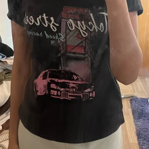 Svart t-shirt med Tokyo streets motiv - Cool svart t-shirt med tryck av en bil och texten 'Tokyo streets speed racing 98'. Perfekt för bilentusiaster och streetwear-stil samt lite 2000s/y2k stil.