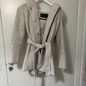 Beige kappa  - Elegant beige kappa från med knappar och ett knytbälte i midjan. Den har en stor krage som ger en stilren look. Varm och är perfekt för höst och vinter! Använd i bra skick!🤍🤍
