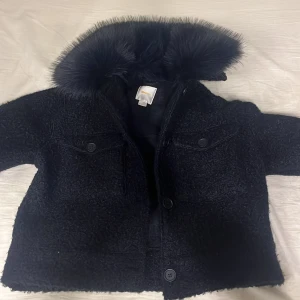 Svart jacka med fuskpäls från Gina Tricot - Säljer en snygg svart jacka från Gina Tricot med fuskpälsdetaljer på kragen. Jackan har knappar framtill och två fickor med knappstängning. Perfekt för kyliga dagar när du vill vara både varm och stilren. 🖤