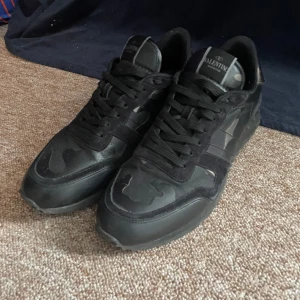 Valentino rockrunners - Snygga svarta sneakers från Valentino med kamouflagemönster och snörning. Perfekta för en stilren look med en touch av edge. Skorna har en robust sula och är märkta med Valentino på tungan och sulan. ÄKTHETSBEVIS FINNS, priset är som alltid diskuterbart mina vänner