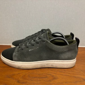 Grå sneakers från Paul Smith - Ett par feta mörkgröna  sneakers från Paul Smith med vita sulor. Skorna har en stilren design med märkets logga på sidan. Perfekta för en avslappnad stil. Storlek 42. Nypris 2400kr 