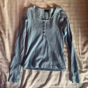 Ljusblå långärmad topp från Gina Tricot - Säljer en ljusblå långärmad topp från Gina Tricot. Toppen har en rund halsringning och knappar framtill. Perfekt för en avslappnad stil. kan säljas tillsammans med den bruna för ett lägre paketpris! storlek m men passar även s.