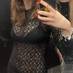 Svart spetstopp - Snygg svart spetstopp med långärmad design. Perfekt för en kväll ute eller en speciell tillställning. Blusen har ett genomskinligt mönster som ger en elegant och trendig look.