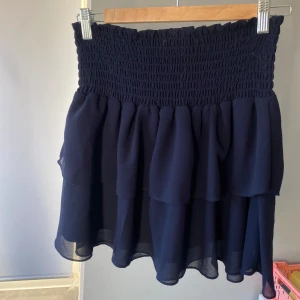 Mörkblå kjol med volang - Marinblå volangkjol från Chelsea. Storlek S. Säljer för att den inte kommer till användning längre. 