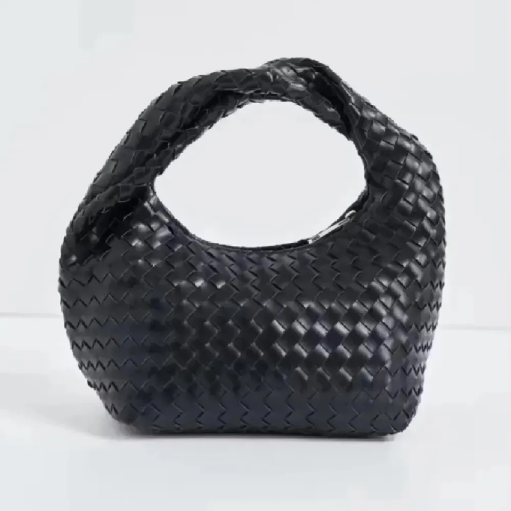 MÖTS BARA UPP Snygg svart handväska med flätat mönster och dragkedja. Perfekt för att ge en stilren touch till din outfit. Väskan har ett bekvämt handtag och är tillverkad i ett elegant material.. Laukut & Käsilaukut.