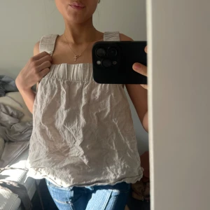 Beige linnetopp - Säljer en stilren beige linnetopp med breda axelband. Toppen har en luftig passform och är perfekt för varma dagar. Den är tillverkad i ett lätt och bekvämt material som ger en avslappnad look.