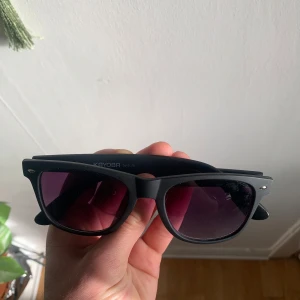 Svarta solglasögon från KAYOBR - Snygga svarta solglasögon från KAYOBR med en klassisk design. De har en matt svart båge och mörka linser som ger ett coolt och stilrent intryck. Perfekta för soliga dagar och en stilren look.