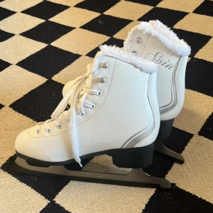 Vita skridskor - Säljer ett par vita skridskor från Revolution i storlek 37. De har en mysig fuskpäls runt kanten och snörning framtill. Knappt använda, kanske 2-3 gånger. Inga skador