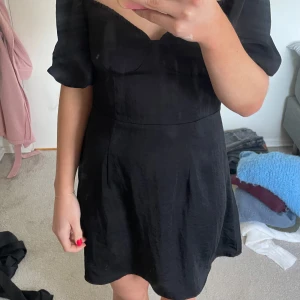 Svart klänning med puffärmar - Snygg svart klänning med puffiga kortärmar och en smickrande passform. Klänningen har en v-ringad design och är perfekt för en stilren look.