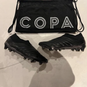 Svarta fotbollsskor från Adidas - Snygga svarta fotbollsskor från Adidas med en stilren design. Skorna har en strumpliknande passform utan snörning och är tillverkade i skinn för en bekväm känsla på planen. Perfekta för den seriösa fotbollsspelaren. 
