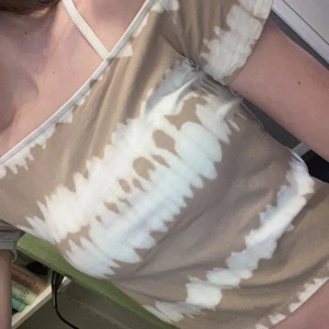 Beige offshoulder topp från H&M - Säljer en snygg beige offshoulder topp från H&M med ett coolt batikmönster i vitt. Toppen har korta ärmar och en avslappnad passform. Perfekt för en avslappnad stil! Magtröja 
