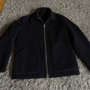 Kort dubbelvävd ulljacka Arket - Snygg svart jacka med dragkedja och stora fickor framtill. Perfekt för en stilren look. Jackan har en klassisk krage och långa ärmar. Jackan är helt i nyskick knappt använd. Nypris på Arket 2590kr. Jackan är i storlek 44 vilket motsvarar S. 🚨🚨Jackan är för tillfället slutsåld hos Arket.