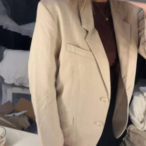 Beige kavaj - Snygg beige randig kavaj med klassisk design och två knappar framtill. Perfekt för en stilren look. Passar bra till både vardag och mer formella tillfällen.