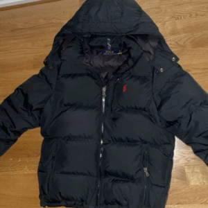 Svart dunjacka från Polo Ralph Lauren - Snygg svart dunjacka från Polo Ralph Lauren med huva och dragkedja. Nästan helt ny, använd ett få tal gånger. Pris kan diskuteras vid snabb affär. 