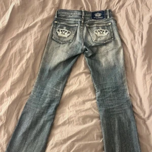Vicktoria Beckham jeans  - Snygga blå jeans med unikt kronbroderi på bakfickorna. De har en klassisk femficksdesign och en knappgylf. Perfekta för en stilren look med en touch av elegans.