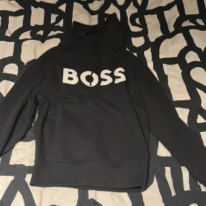 Svart hoodie från BOSS - Säljer en stilren svart hoodie från BOSS med stor vit logga på framsidan. Nypris 2099 . Skick 10/10 helt ny.fick den i julklapp och den var förliten. Skirv vid frågor och funderingar. 