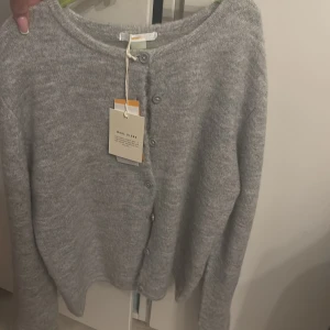 Grå kofta från Gina Tricot - Mysig grå kofta från Gina Tricot i ullblandning. Den har långa ärmar och knappar framtill. Säljer pga jag köpte två i olika storlekar o andvänder då bara en utav dem. Super najs kofta! 