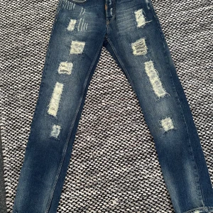 Adrian hammond jeans med slitningar - Snygga blå jeans med coola slitningar på framsidan. De har en broderad design på baksidan 