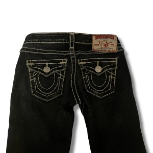 True religion jeans - Snygga True religion jeans med kontrastsömmar. Jeansen är bootcut och lågmidjade. Ett litet hål på knäet som ska vara där som en liten detalj. Inga defekter. [Midjemått: 34cm] [Innerbenslängd: 84cm] Kontakta mig ifall du har några funderingar!