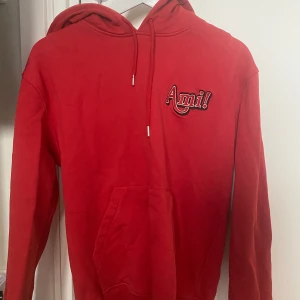 Ami Paris hoodie - Säljer en snygg röd hoodie från Ami med broderad text på bröstet. Den har en klassisk design med huva och känguruficka framtill. Perfekt för en avslappnad stil.