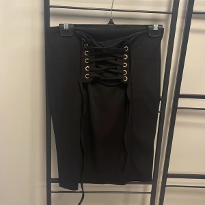 Svart kjol med snörning från Bubbleroom - Snygg svart kjol från Bubbleroom med cool snörningsdetalj framtill. Kjolen har en tight passform och är perfekt för att ge en edgy touch till din outfit. Tillverkad i ett mjukt och bekvämt material.