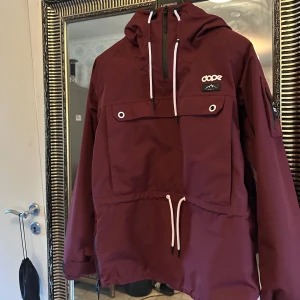 Vinröd jacka från Dope - Säljer en snygg vinröd jacka från Dope med huva och dragkedjan är på sidan går fån hand till slutet så man kan öppna hela sidan så de e änkelt å ta av å på. Jackan har en praktisk ficka på bröstet och justerbar dragsko i midjan. Perfekt för kyligare dagar. Helt oanvänd 