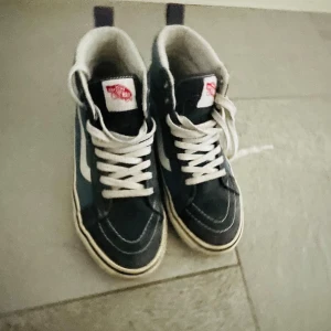 sneakers från Vans - Snygga sneakers från Vans. Skorna har en klassisk hög modell med det ikoniska sidostrecket i vitt. Perfekta för en avslappnad stil. Lite sliten men annars inga defekter🌟