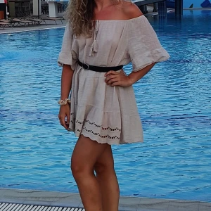 Beige offshoulder klänning med spetsdetaljer - Charmig beige offshoulder klänning med korta ärmar och vackra spetsdetaljer vid fållen. Den har en avslappnad passform. Perfekt för varma sommardagar vid poolen eller stranden.