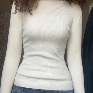 Vit ribbad polotröja - Säljer en stilren vit ribbad polotröja med lång ärm. Perfekt för en elegant och enkel look. Tröjan har en tight passform på mig som har M vanligtvis.