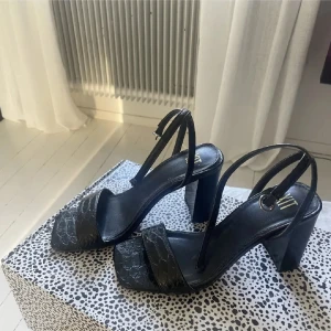 Svarta sandaler med klack - Eleganta svarta sandaler med bred klack och smala remmar. Skorna har en subtilt mönstrad yta som ger en extra touch av stil. Perfekta för en kväll ute eller en speciell tillställning. Storlek 37 och använda två gånger💕