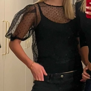 Svart prickig blus - Snygg svart blus med prickigt mönster och transparenta ärmar. Blusen har en elegant design med korta ärmar och rund halsringning. Perfekt för en stilfull look.(linnet ingår inte!) storlek L men passar mer som S-M