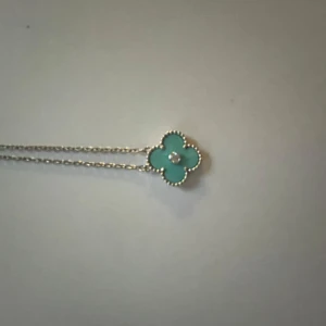 Halsband från Van Cleef & Arpels - Elegant halsband från Van Cleef & Arpels med en fyrklöverformad berlock. Berlocken har en turkos färg med en diamant i mitten och är omgiven av en fin silverkant. Perfekt för att ge en touch av lyx till din stil.